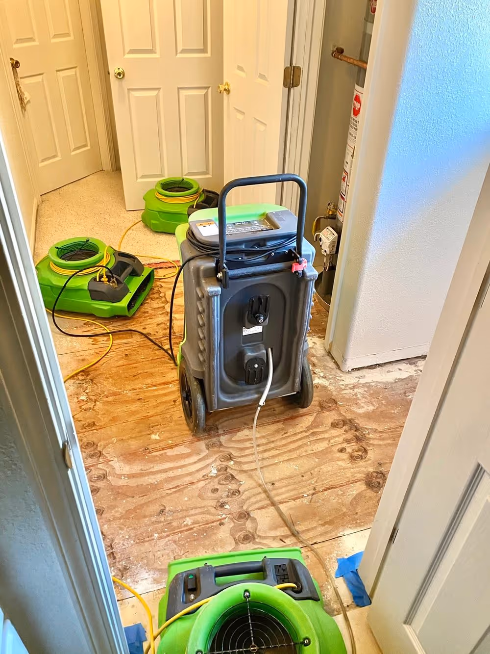 Air movers and a dehumidifier running in a doorway during a structural dry-out