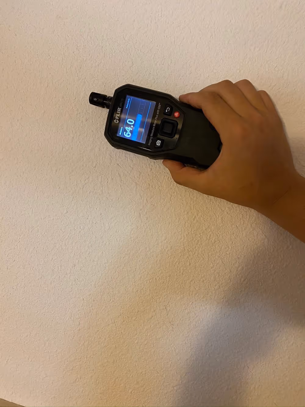A moisture meter held against a wall during an inspection