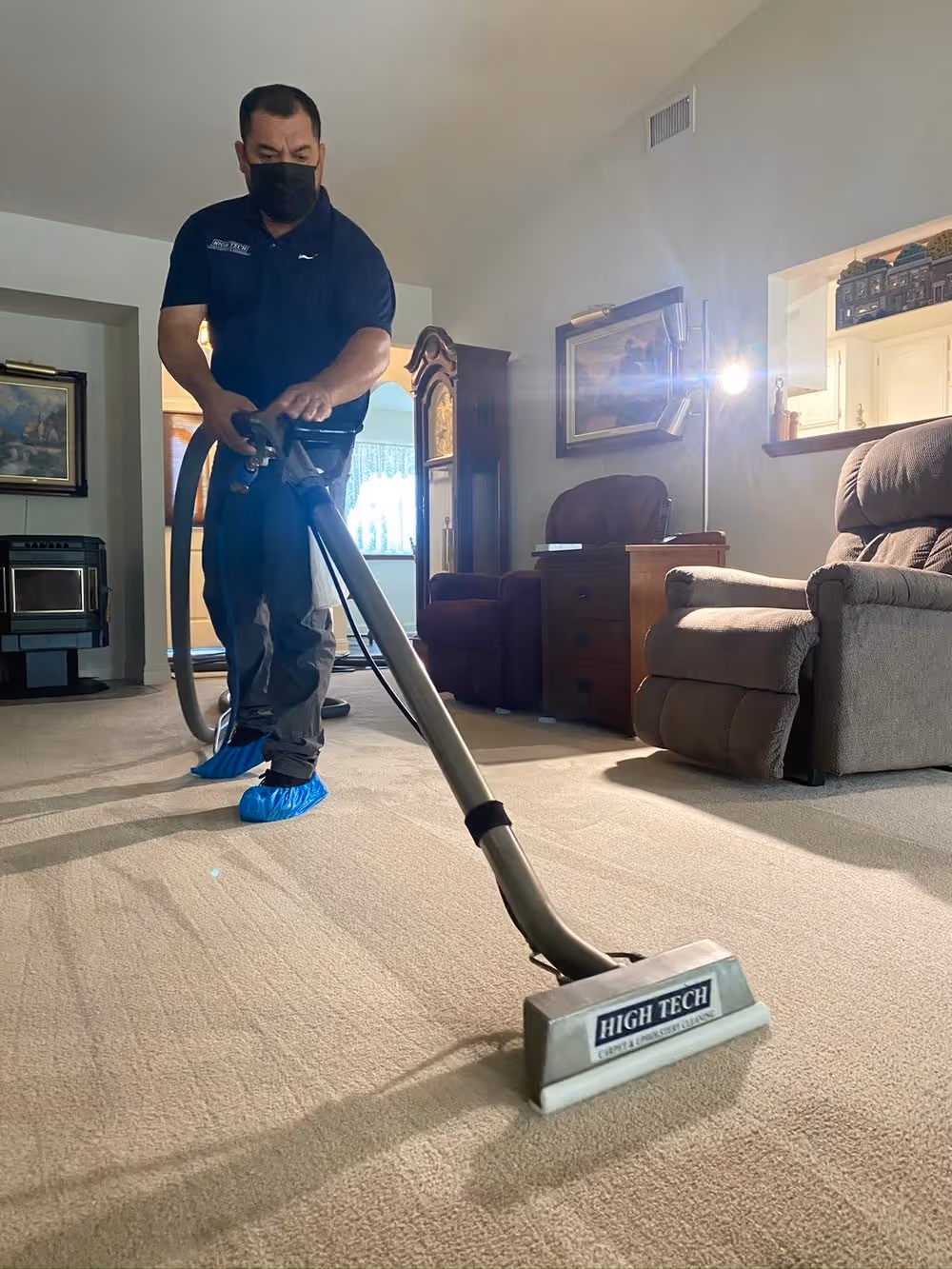 A High Tech technician running the extraction wand across a living-room carpet